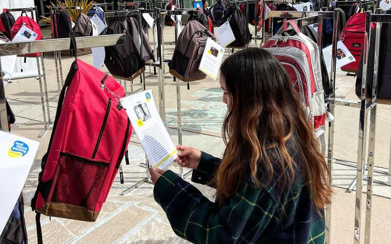 Girl reading a note on one of hundreds of backpacks hanging on display.