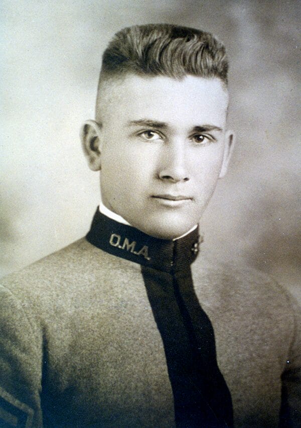A vintage photograph of a young man wearing a military uniform, smiling and standing proudly.