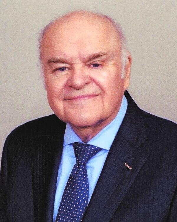 An older man in a suit and tie smiles warmly at the camera, exuding confidence and professionalism.