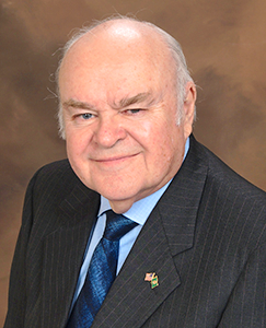 A man in a suit and tie smiles while posing for a professional photo.