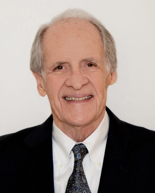 An older man in a suit and tie smiles warmly at the camera, exuding confidence and professionalism.