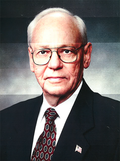 A man wearing a suit and tie, with glasses, stands confidently, exuding professionalism and style.