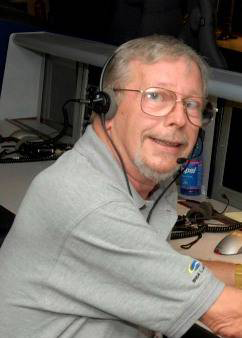 A man wearing a grey shirt and headphones is focused on working at a computer.