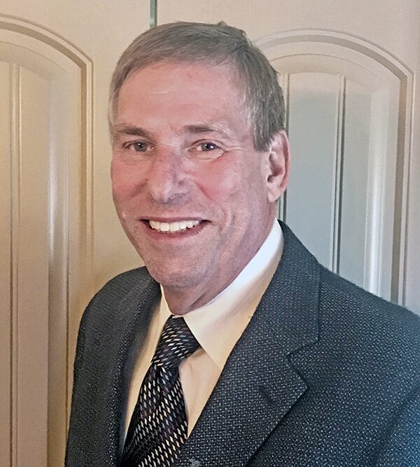 A man in a suit and tie smiles confidently at the camera, exuding professionalism and approachability.