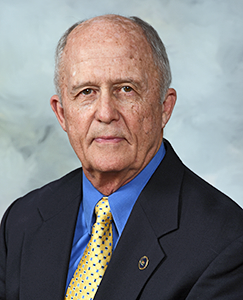 A man in a suit and tie seated against a solid blue background, exuding professionalism and confidence.