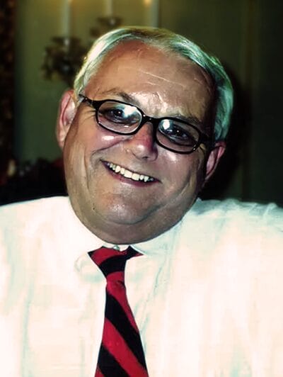 A man with glasses wearing a red tie, looking confidently at the camera.