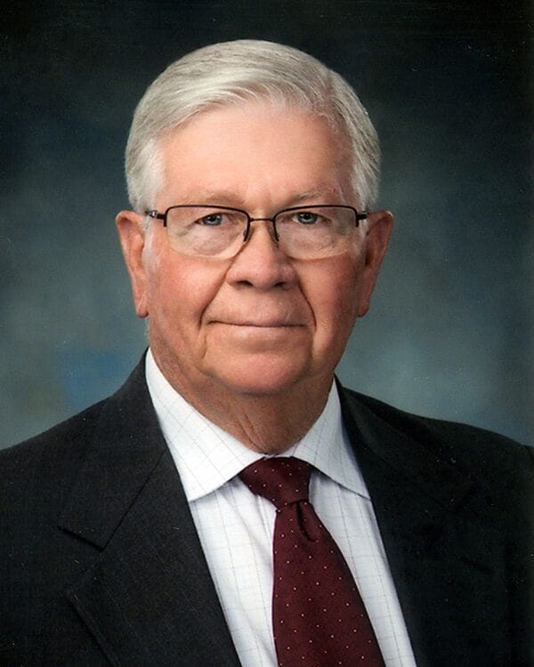 A man wearing a suit and tie, with glasses, stands confidently, exuding professionalism and sophistication.