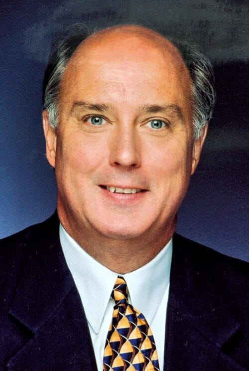 A man in a suit and tie stands confidently in a well-lit room, exuding professionalism and poise.