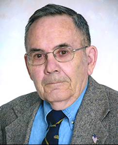 An older man with glasses and a tie, smiling and looking directly at the camera.