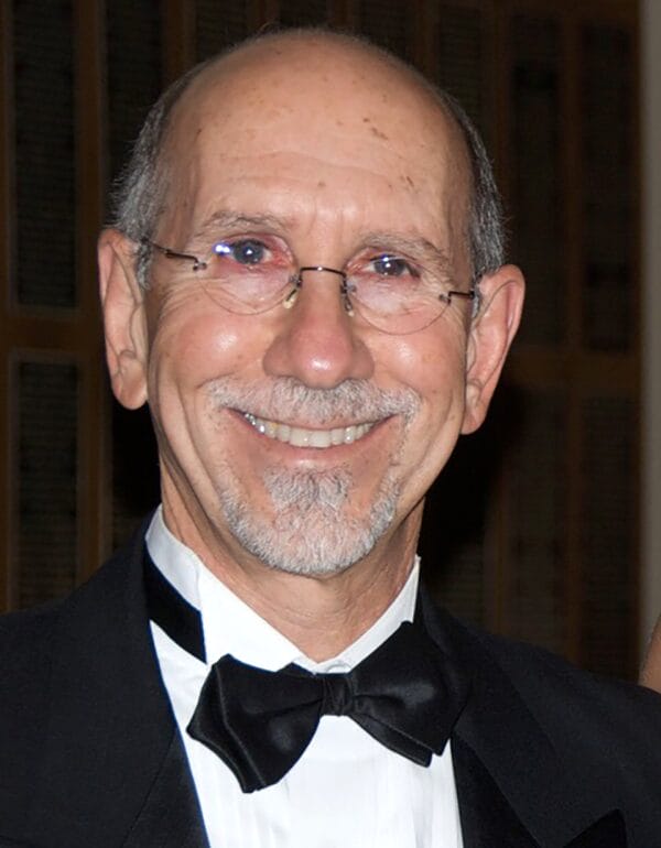 A man in a tuxedo and bow tie smiles confidently, exuding elegance and charm.