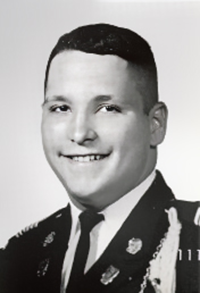 A black and white photo of a man in military uniform, standing confidently with a serious expression.