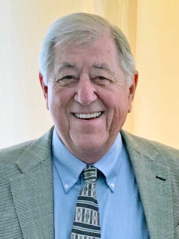 A man in a suit and tie is seated, looking confidently at the camera in a professional setting.