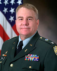 A man in a military uniform stands confidently, showcasing his attire and insignia against a neutral background.