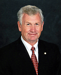 A man in a suit and tie smiles while posing for a photo, showcasing a professional appearance.