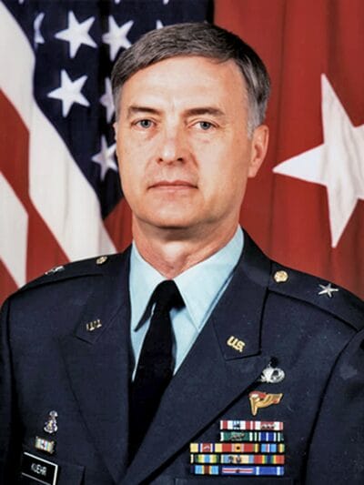 A man in military uniform stands proudly in front of an American flag, symbolizing patriotism and service.