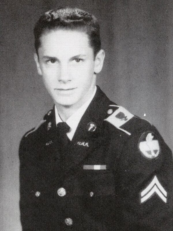 A young man in a military uniform smiles while posing for a photo.