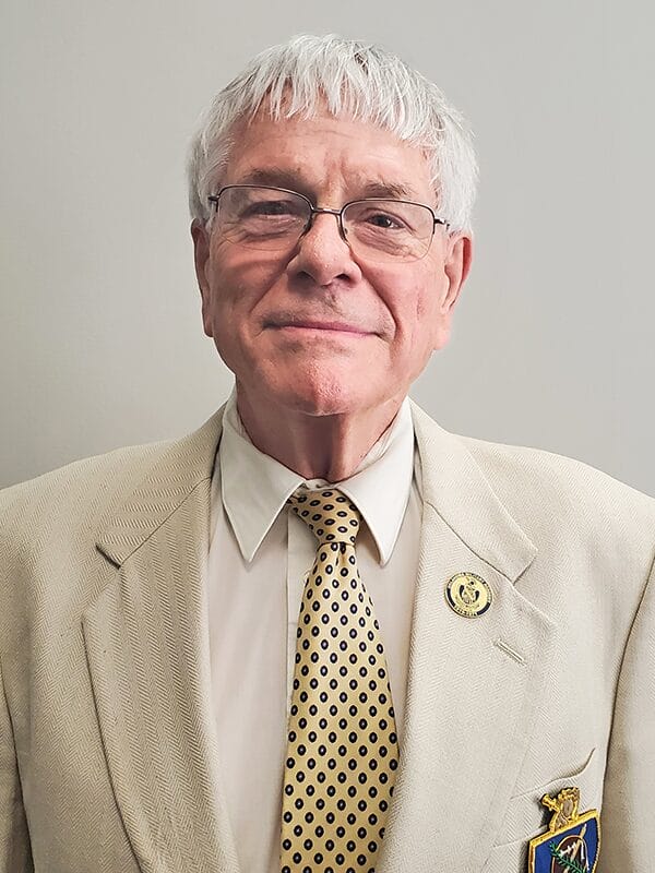 A man wearing a suit and glasses, with a yellow tie, stands confidently, showcasing a professional appearance.
