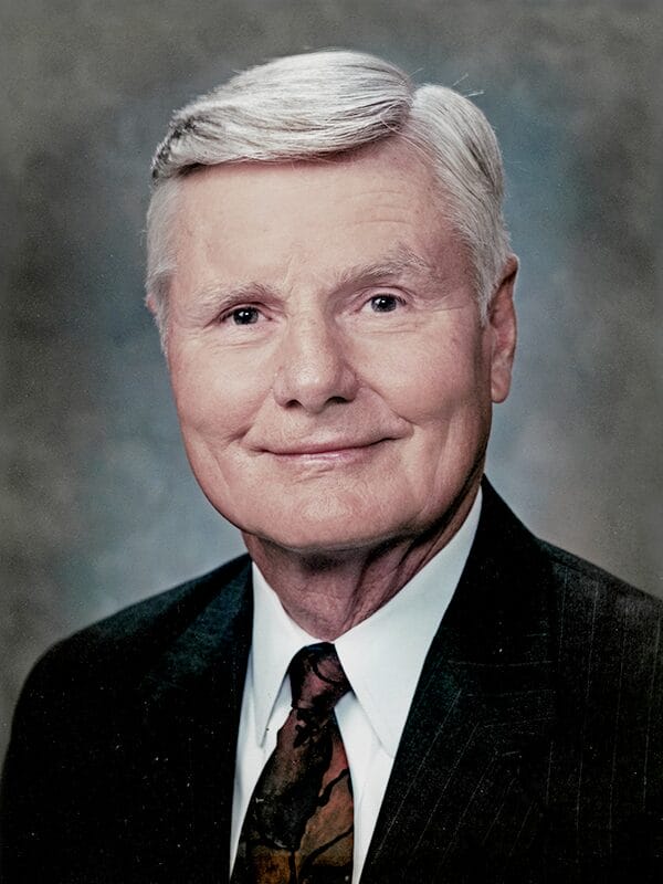 Older white male sitting for a professional headshot. He has white hair parted to the side. He is wearin ga suit and tie.