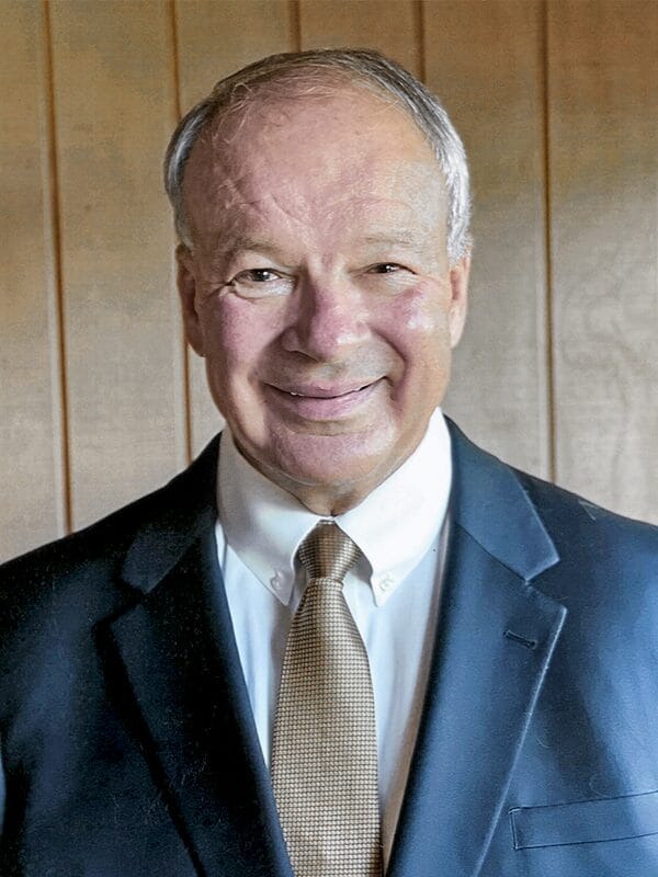 A man in a suit and tie smiles confidently at the camera, exuding professionalism and approachability.