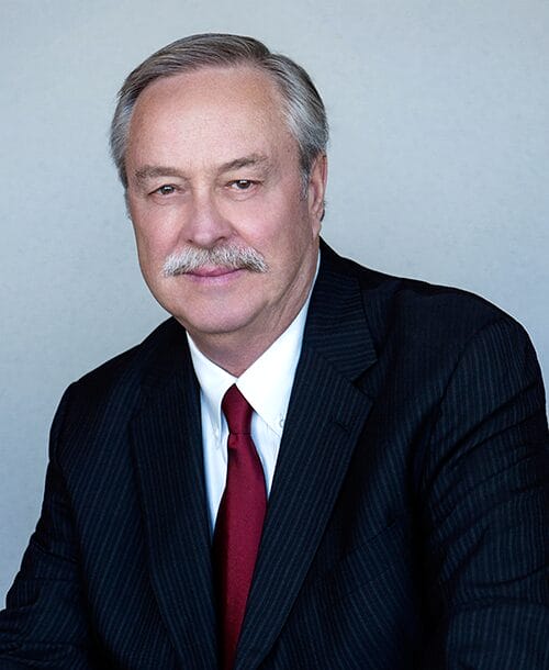 A man in a suit and tie stands confidently in a well-lit room, exuding professionalism and poise.