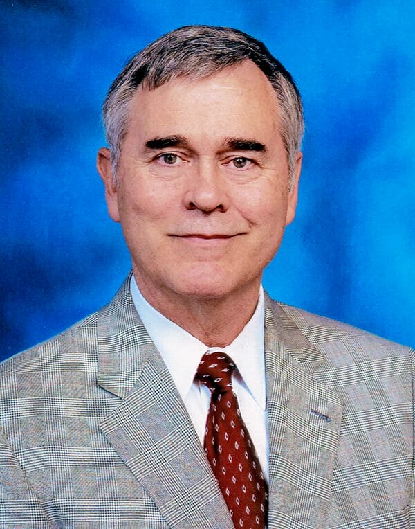 A man in a suit and tie stands confidently, smiling for the camera in a professional photo setting.