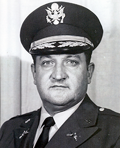 A black and white photo of a man in military uniform, standing confidently with a serious expression.