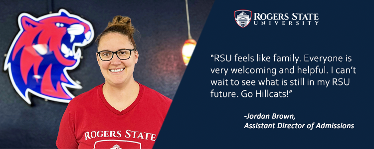 Girl wearing Rogers State shirt standing in front of Hillcat head.