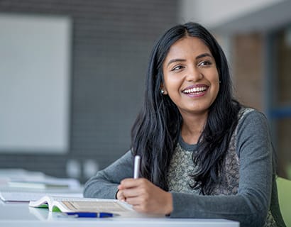 student smiling while writing in a notebook at a desk in a classroom
