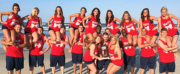 Cheer squad posing on the beach with their trophy.