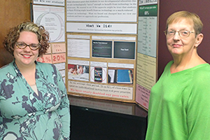 Two instructors standing by their poster presentation.