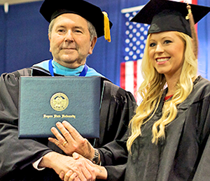 President Rice shaking hand and giving diploma to a student.