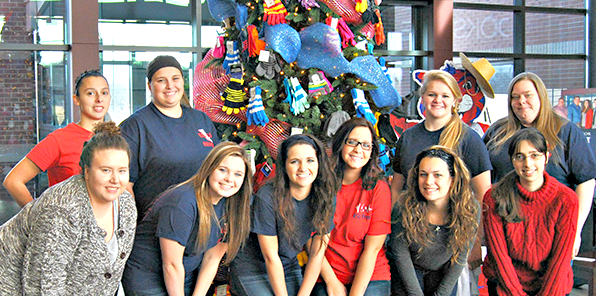 Students posing in front of Christmas tree decorated with mittens.