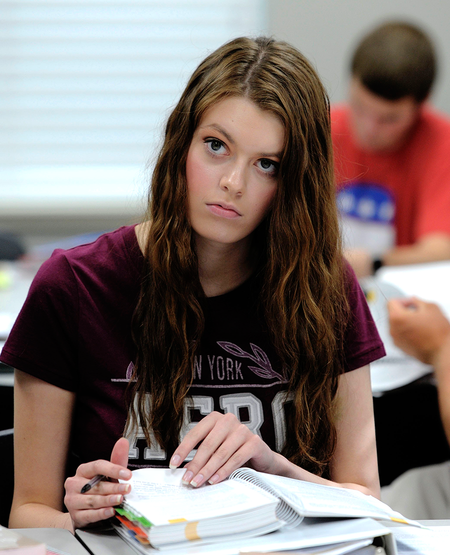 Girl in class listening to a lecture and taking notes.
