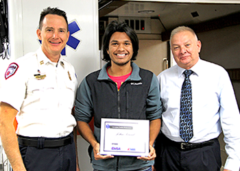 Student holding certificate with instructor and paramedic.