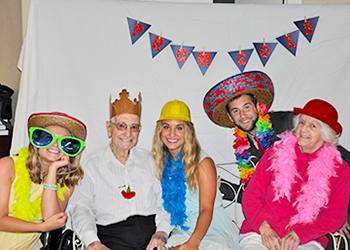 RSU students posing with seniors in sill hats, large sunglasses, and feather boas under a Prom 2015 banner.