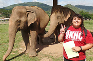 Layna holding up the peace sign with elephants behind her.