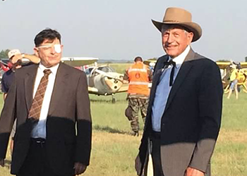 Two men standing in field by airplanes.