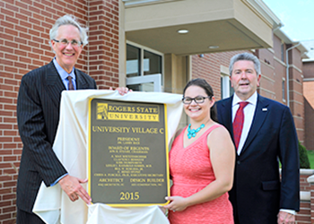 People standing next to building plaque.