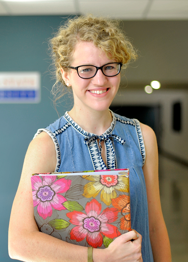 Girl in hallway holding a notebook with flower print.