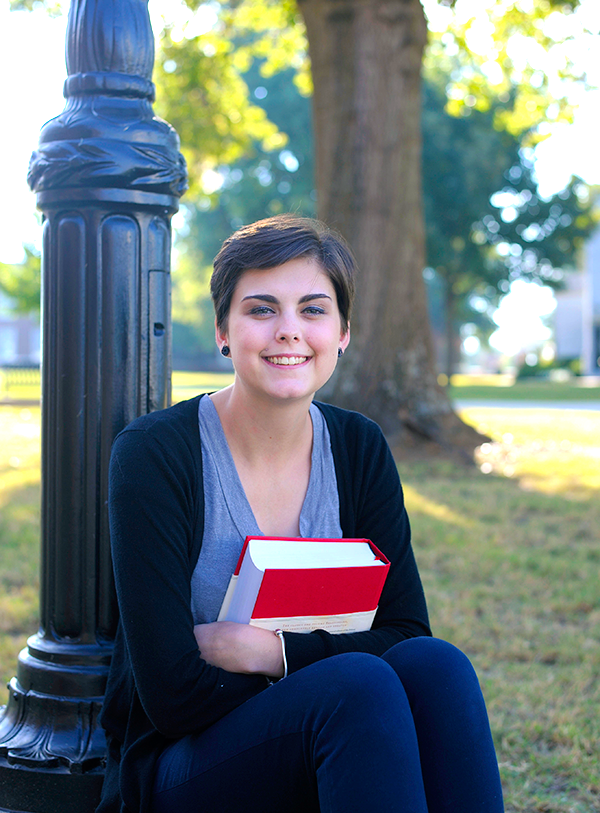 Girl sitting under lamp post holding school book.