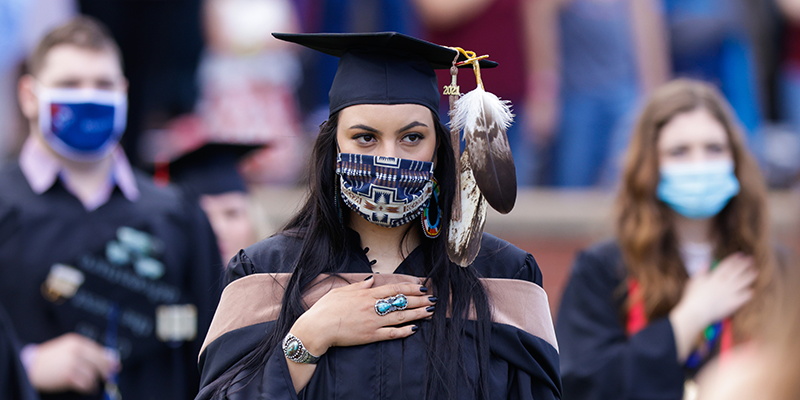 Girl in cap and gown with hand on heart and feather hanging from cap.