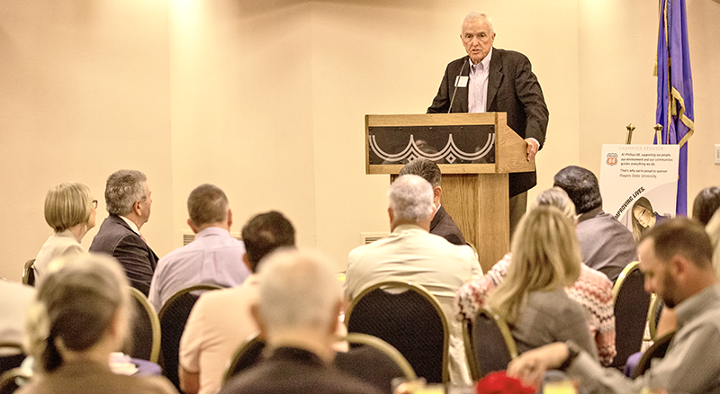 man at podium speaking to audience at tables