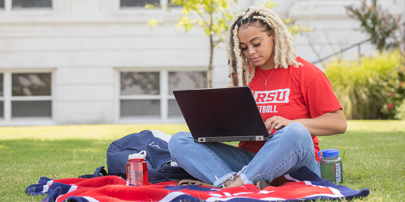 Girl sitting on blankout outside working on laptop