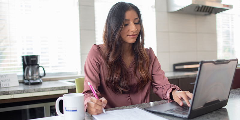 girl taking notes on paper looking at laptop