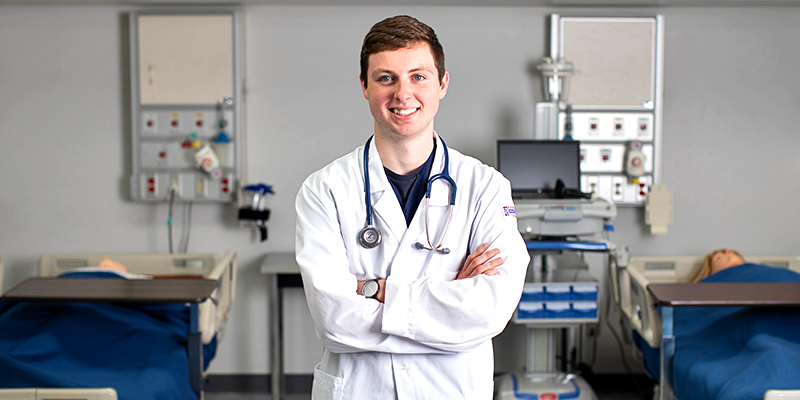 Male student wearing white coat with a stethoscope.