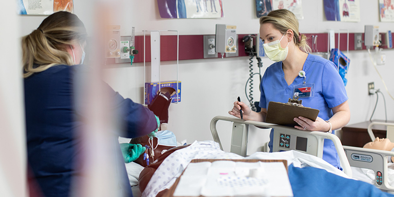 girl in mask and scrubs taking notes next to patient bed