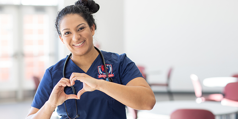 Girl in scrubs with hands in shape of heart
