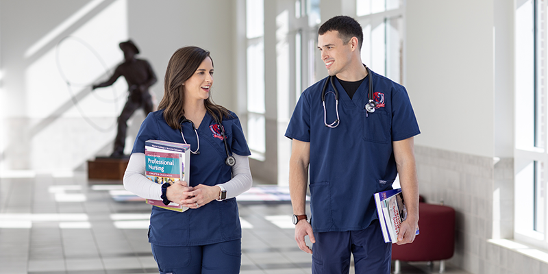 Boy and girl in scrubs walking in hallway carrying books