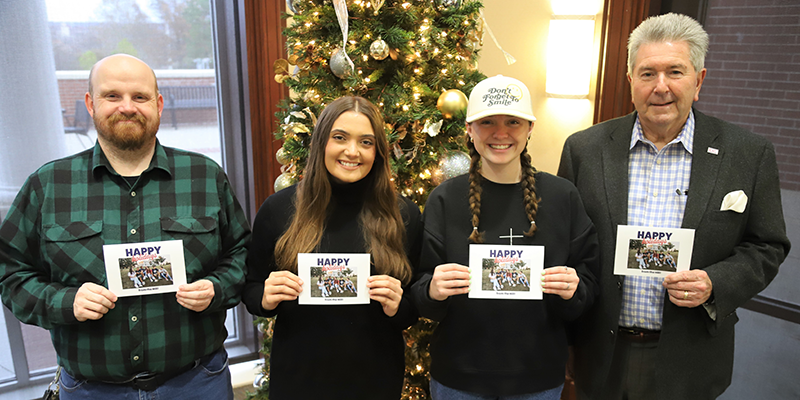 group in front of Christmas tree holding cards