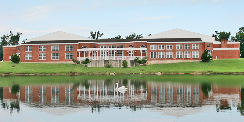 Brick building with white columns and swan on a lake in front.